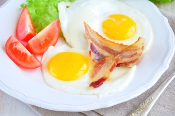 fried eggs with bacon and tomato slice on a white plate