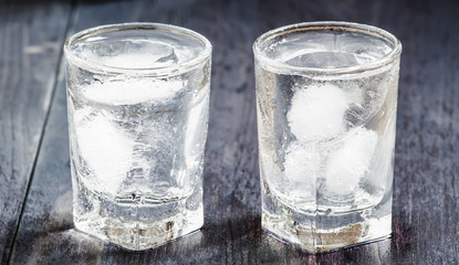 Clold fresh water with ice in a glass on a dark background in vi