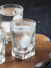 Clold fresh water with ice in a glass on a dark background in vi