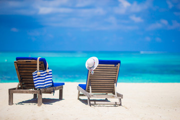 Lounge chairs with bag and hat on tropical white beach 