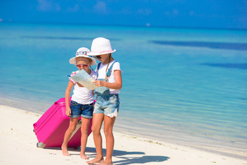 Little girls with big suitcase and map at tropical beach