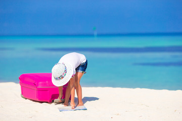 Fototapeta na wymiar Little adorable girl with big suitcase on tropical white beach 