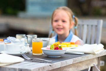 Adorable little girl having breakfast at outdoor cafe