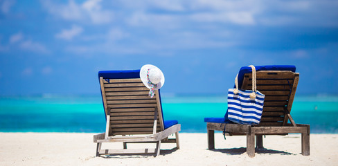 Lounge chairs with bag and hat on tropical white beach 
