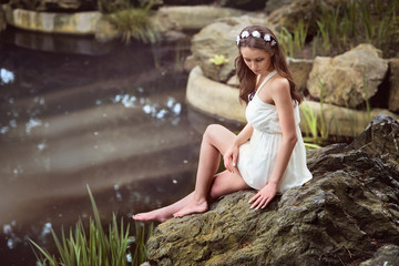 Beautiful woman  wearing white dress sitting near a lake