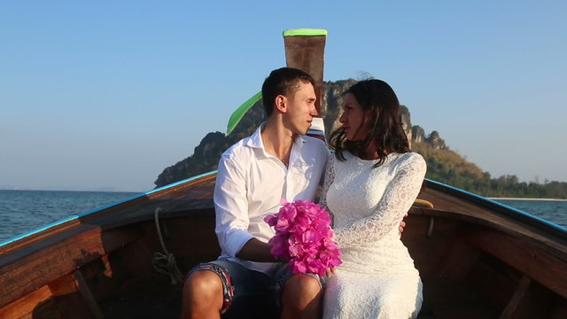 bride and groom float in longtail boat to island at sunrise	