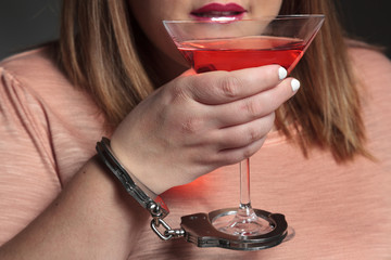 Woman handfuffed to a cosmopolitan cocktail is drinking
