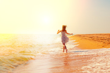 Happy girl running on the beach towards the sun