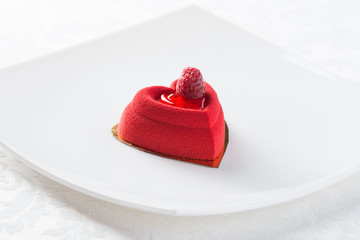 Heart-shaped red dessert with raspberry on white plate