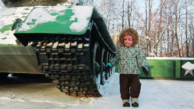 Child walking near A battle tank in the winter
