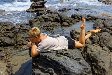 Young woman relaxing and meditating on rocky seashore