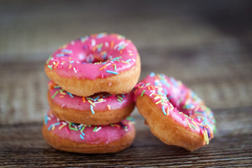 Donuts with pink icing and color sprinkles on wooden background