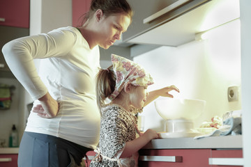 Pregnant mother and her daughter cooking in the kitchen