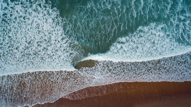 Aerial drone slow motion footage of ocean waves reaching shore. Lockdown shot of sea waves creating a texture from the white sea foam. HD 1080 video.