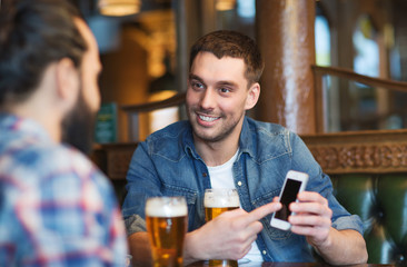 male friends with smartphone drinking beer at bar