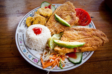 Breaded fish served with rice and plantain chips, traditional
