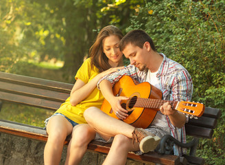 Young couple in love playing acoustic guitar in the park
