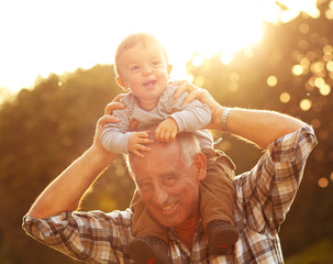 Grandfather carrying grandson on shoulders in park