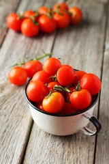 Fresh cherry tomatoes in cup on grey wooden background