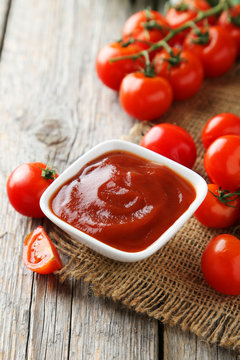 Fresh tomatoes with bowl of ketchup on  wooden background