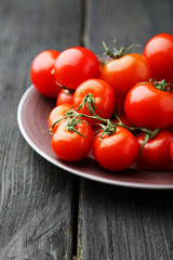 Fresh cherry tomatoes in plate on black wooden background