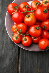 Fresh cherry tomatoes in plate on black wooden background