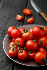 Fresh cherry tomatoes in plate on black wooden background
