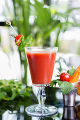 bright summer refreshing alcoholic cocktail Bloody Mary on a table in a restaurant with a creative decoration of cherry pepper greens. soft focus