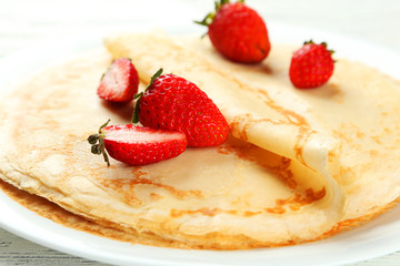 Pancakes with strawberry on plate on white wooden backgound