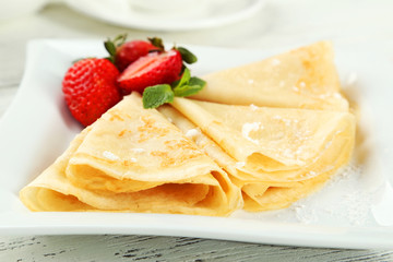 Pancakes with strawberry on plate on white wooden backgound
