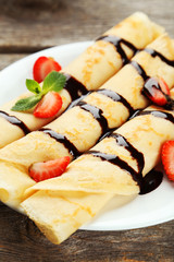 Rolled pancakes with strawberry on plate on wooden background