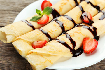 Rolled pancakes with strawberry on plate on wooden background