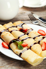 Rolled pancakes with strawberry on plate on  wooden background