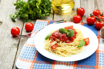 Spaghetti with tomatoes and basil on plate on grey wooden backgr