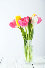 Beautiful tulips in vase on white wooden background