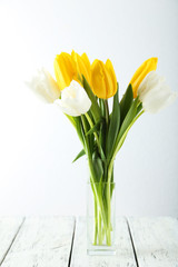 Beautiful tulips in vase on white wooden background