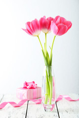 Beautiful tulips in vase on white wooden background