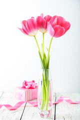 Beautiful tulips in vase on white wooden background