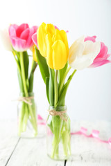 Beautiful tulips in vase on white wooden background