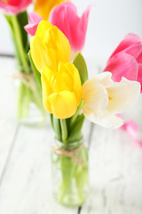 Beautiful tulips in vase on white wooden background