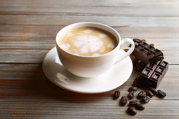 Cup of coffee latte art with grains and chocolate bar on wooden table background