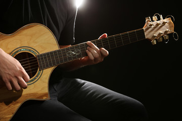 Obraz na płótnie Canvas Young man playing on acoustic guitar on dark background