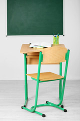 Wooden desk with stationery and chair in class on blackboard background