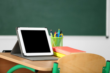 Wooden desk with stationery and tablet in class on blackboard background