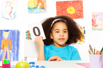 African girl holds flashcard with zero at  desk