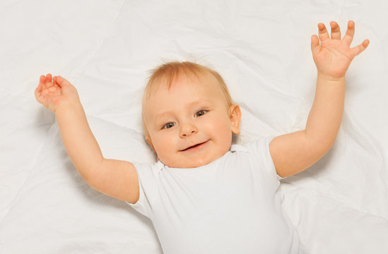 Chubby small baby with arms up on white blanket