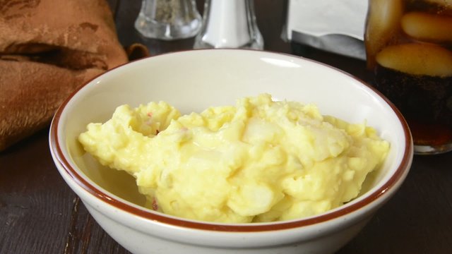 Spooning mustard potato salad into a bowl
