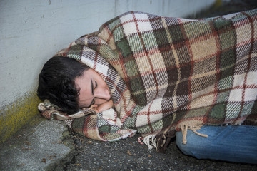Young male beggar on city sidewalk sleeping