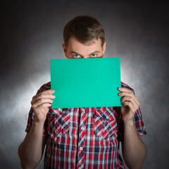 Naklejka premium Young man holding green blank paper on dark grey background.