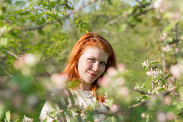 beautiful red-haired girl walks in apple orchard